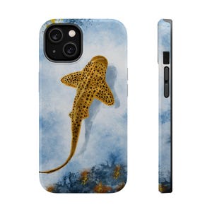 May include: A watercolor illustration of a spotted shark swimming in blue water. The shark is yellow with brown spots and has a long tail. The background is a light blue watercolor wash with hints of yellow and orange.
