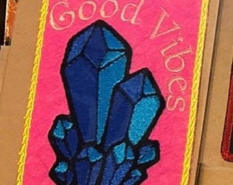 May include: Embroidered patch with a pink background and a yellow border. The patch features a cluster of blue crystals and the words "Good Vibes" in a cursive font.