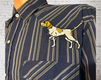 May include: A blue and white striped long-sleeved shirt with a brown and white dog embroidered on the left chest. The shirt has a button-down collar and a single chest pocket.