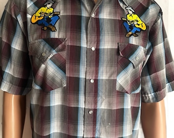 May include: A plaid button-down shirt with short sleeves and two embroidered patches of a cartoon cowboy playing a guitar on each side of the chest.