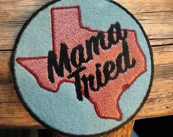 May include: Round patch with a light blue background and a red embroidered outline of the state of Texas. The words "Mama Tried" are embroidered in black script across the Texas outline.