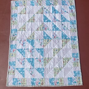 May include: A handmade patchwork quilt. It features white squares and triangles in shades of blue and green, with patterned fabrics. The border has a light green and white pattern. The quilt is machine quilted.