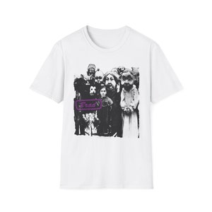 以下が含まれることがあります： 白いTシャツに、マスクをつけた人々のグループの白黒のグラフィックプリントが施されています。白い長方形に紫色の文字で「Brad」と印刷されています。