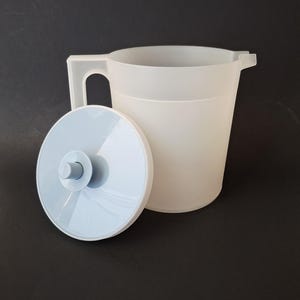 May include: A white plastic pitcher with a handle and a light blue lid. The lid is off to the side, revealing the pitcher's opening. The pitcher is designed for liquids and is likely used for serving beverages.