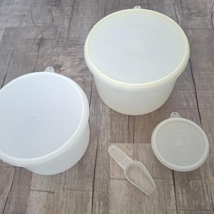 May include: A collection of off-white plastic food storage containers with lids and a small scoop. The containers are round and vary in size. The lids have a small tab for easy opening. The scoop is small and has a scoop shape.