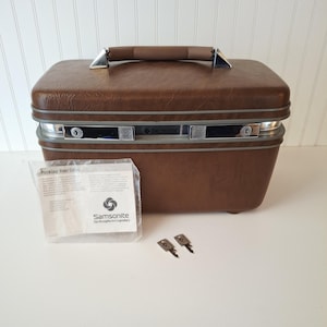 May include: A brown Samsonite vanity case with a silver trim and handle. The case has two locks and comes with two keys and a packing guide. The Samsonite logo is visible on the case and the packing guide.