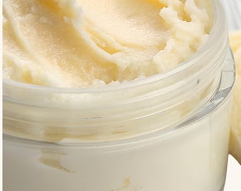 Può includere: Un barattolo di plastica trasparente e rotondo riempito con una sostanza cremosa, densa e di colore giallo pallido. La consistenza della crema è visibile con morbidi picchi e vortici, indicando una densità liscia. Il barattolo ha un design semplice.