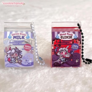 Könnte beinhalten: Zwei transparente Acryl-Anhänger in Form von Milchkartons. Einer zeigt "Sanzu River MILK" mit einer Cartoonfigur und "100% organic!". Der andere zeigt "Blood Pools ELIXIR" mit einer Cartoonfigur und "100% organic!". Beide haben eine Kette.