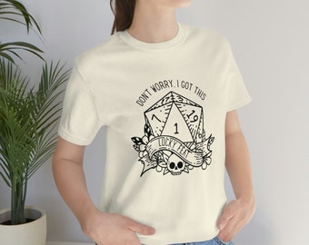 May include: Cream-colored t-shirt featuring a black graphic of a twenty-sided die with the numbers 1, 19, and other symbols. The text "DON'T WORRY, I GOT THIS" arches above the die, and "LUCKY FEAT" is written on a banner below.