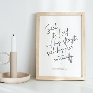 May include: A framed print with a white background and black text that reads "Seek the Lord and his strength, seek his face continually. 1 Chronicles 16:11". The frame is light wood and the print is sitting on a white surface.