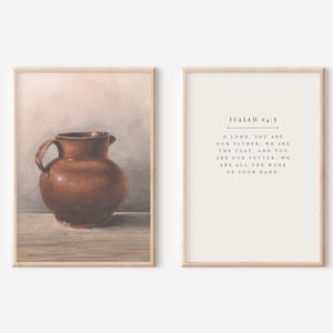 Op de afbeelding: Twee ingelijste kunstdrukken. De linkerprint toont een bruine keramische kruik op een houten oppervlak. De rechterprint heeft de tekst "ISAIAH 64:8" en een citaat. Beide prints zitten in lichte houten frames.