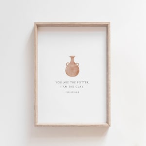 May include: Framed art print featuring a watercolor illustration of a brown vase with handles. The print includes the text "YOU ARE THE POTTER, I AM THE CLAY. ISAIAH 64:8" in a minimalist style. The frame is light brown.