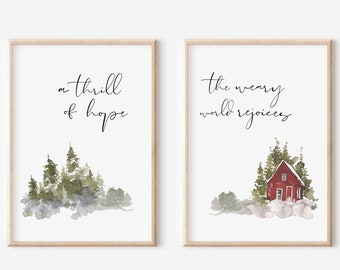 May include: Two watercolor prints with inspirational quotes. The first print features a forest scene with the text "a thrill of hope". The second print features a red cabin in a snowy forest with the text "the weary world rejoices".
