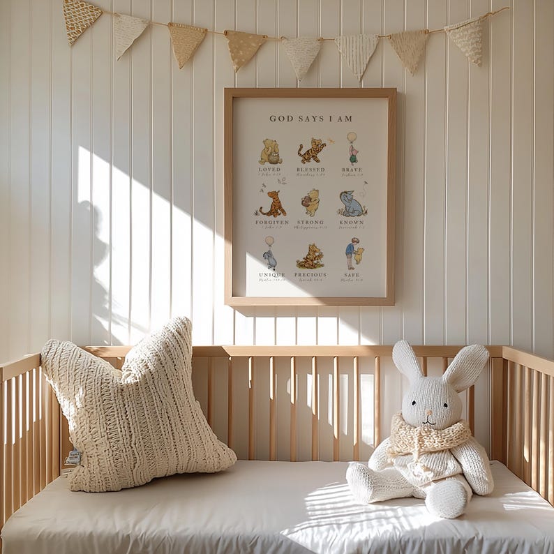 May include: A Winnie the Pooh themed nursery decor print with the text "God Says I Am" and a list of positive affirmations. The print is framed in a light brown wood frame and is hanging on a white wall with a white wood paneling.