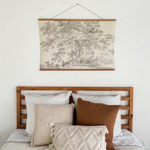 Puede incluir: Un dormitorio con cabecero de madera y una cama cubierta con un edred&oacute;n blanco. Cojines decorativos en tonos crema y marr&oacute;n est&aacute;n colocados sobre la cama. Una impresi&oacute;n enmarcada de un &aacute;rbol, con el texto "ROOTED & GROUNDED IN LOVE", cuelga sobre la cama.