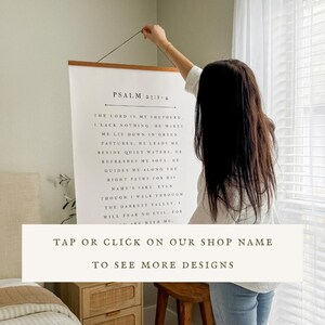 May include: A large, rectangular wall hanging with the text of Psalm 23:1-4 printed in black on a white background. The text is displayed in a classic serif font. The hanging is suspended by a wooden rod and a brown string. The bottom of the hanging has the text: "TAP OR CLICK ON OUR SHOP NAME TO SEE MORE DESIGNS."