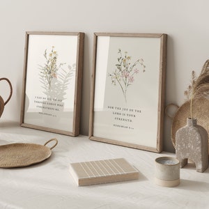 May include: Two framed art prints with floral designs and inspirational quotes. The prints have light wood frames and feature botanical illustrations in soft colors. One print reads "I CAN DO ALL THINGS THROUGH CHRIST WHO STRENGTHENS ME." The other reads "FOR THE JOY OF THE LORD IS YOUR STRENGTH."