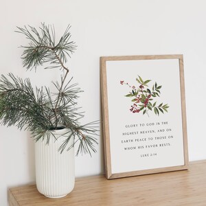 May include: A framed print with a white background and a floral illustration of red berries and green leaves. The print includes the text "Glory to God in the highest heaven, and on earth peace to those on whom his favor rests. Luke 2:14".