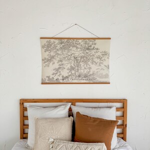 Puede incluir: Un dormitorio con cabecero de madera y una cama adornada con almohadas de diversas texturas y colores. Sobre la cama, un gran cuadro enmarcado de un &aacute;rbol, con el texto "ROOTED & GROUNDED IN LOVE". Las almohadas son de tonos blancos, crema y marr&oacute;n.