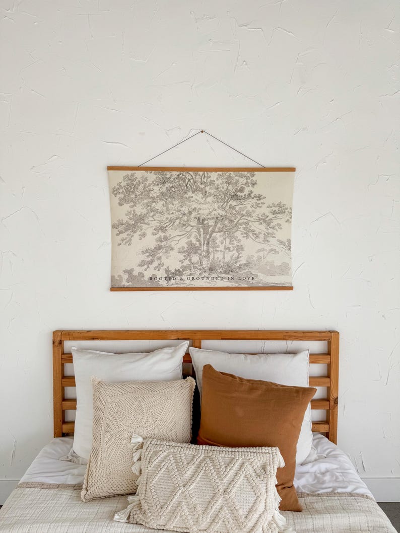 Puede incluir: Un dormitorio con cabecero de madera y una cama adornada con almohadas de diversas texturas y colores. Sobre la cama, un gran cuadro enmarcado de un &aacute;rbol, con el texto "ROOTED & GROUNDED IN LOVE". Las almohadas son de tonos blancos, crema y marr&oacute;n.
