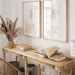 May include: Two framed art prints with floral arrangements and inspirational quotes. The prints are displayed above a wooden console table with books and decorative items. The room has a neutral colour palette with natural light.