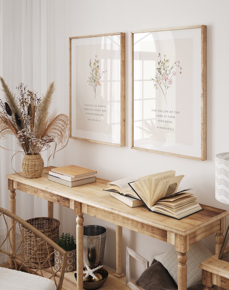 May include: Two framed art prints with floral arrangements and inspirational quotes. The prints are displayed above a wooden console table with books and decorative items. The room has a neutral colour palette with natural light.