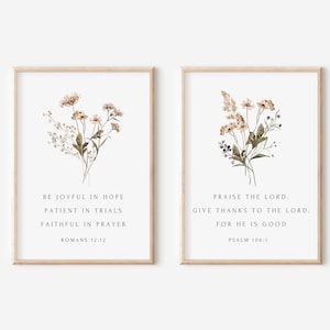 May include: Two framed art prints with floral arrangements. The left print features text from Romans 12:12, and the right print features text from Psalm 106:1. The frames are light brown, and the background is white.