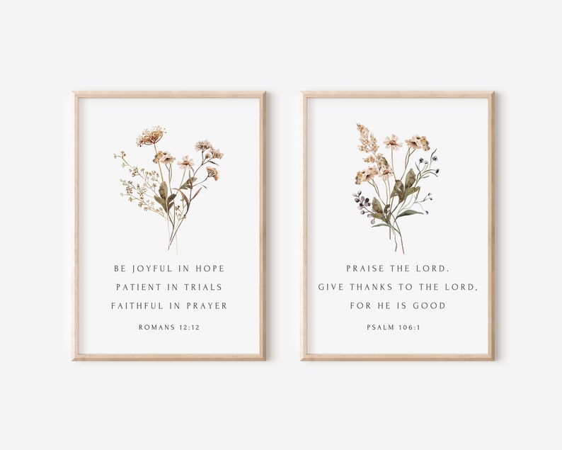 May include: Two framed art prints with floral arrangements. The left print features text from Romans 12:12, and the right print features text from Psalm 106:1. The frames are light brown, and the background is white.