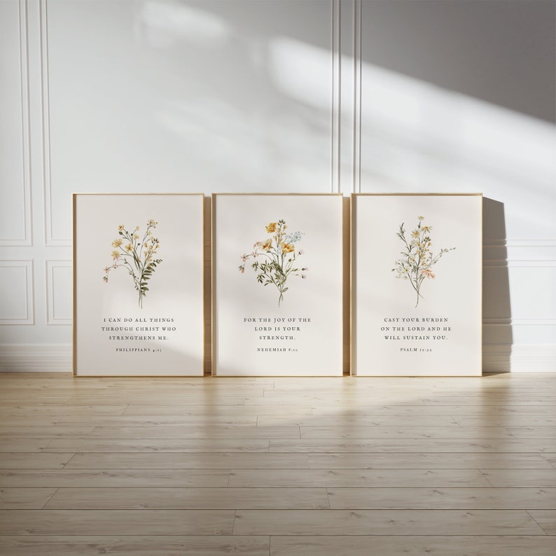 May include: Three framed art prints with botanical illustrations and inspirational quotes. Each print features a gold frame, a cream-colored background, and a different floral arrangement in yellow, white, and green. The text includes Bible verses.