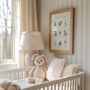 May include: A white crib with a white lamp and a stuffed animal in the shape of a bunny. The crib has a white blanket and a pink pillow. A framed print with the text "God Says I Am" is hanging on the wall.