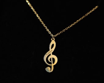 Puede incluir: Un collar de oro con un colgante de clave de sol en una caja de terciopelo negro. El colgante tiene la palabra "Kailyn" grabada.
