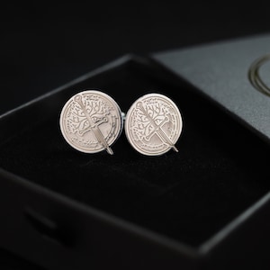 May include: A pair of silver cufflinks with a tree and sword design in a black box.