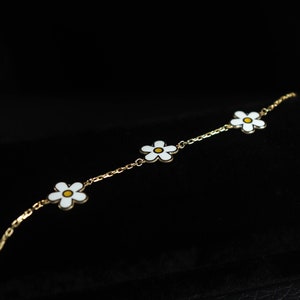 May include: A delicate gold chain bracelet with three white enamel daisy charms. Each daisy has a yellow center.