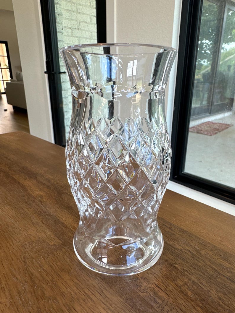 May include: A clear glass vase featuring a flared rim and a tapered base. The body of the vase is decorated with a prominent diamond-shaped cut pattern that covers the midsection, creating a textured, faceted appearance throughout the glass surface.