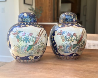 Puede incluir: Dos jarrones de porcelana azul y blanco con detalles dorados y diseños florales y de pájaros. Los jarrones tienen tapas y están decorados con una variedad de colores, incluyendo rojo, amarillo, verde y azul.
