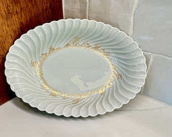 May include: A white ceramic serving dish with a scalloped edge and gold accents. The dish has a swirl design and is perfect for serving appetizers, desserts, or snacks.