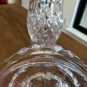 May include: A clear glass vase featuring a prominent diamond-cut pattern across its body and a flared rim. The base of the vase is circular with a starburst design etched into the bottom, showing the Waterford brand name clearly visible in the glass.