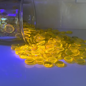 May include: A glass jar filled with yellow glass beads spills onto a blue surface. The beads are round and translucent, with a slight shimmer.