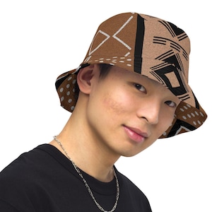 May include: A brown bucket hat with a geometric pattern in black and white. The hat has a wide brim and is made of a textured fabric. The hat is worn by a person wearing a black shirt.