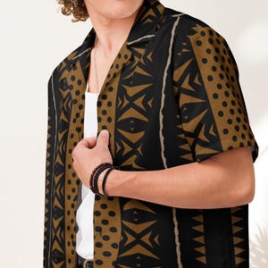 May include: Short-sleeved button-down shirt with a bold geometric pattern in black and gold. The shirt features a collared neckline and is worn over a white undershirt. The design includes triangles, dots, and vertical stripes.