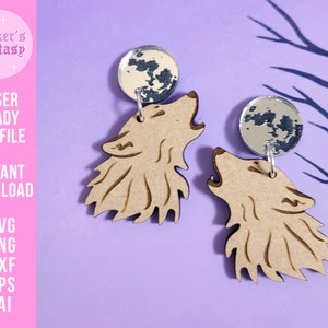 May include: A pair of laser cut wooden earrings featuring a howling wolf silhouette with a silver moon charm. The earrings are on a purple background.