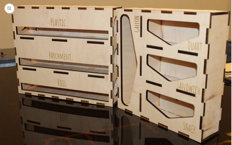 May include: A wooden organizer with labeled compartments for storing different types of food wrap. The compartments are labeled "Plastic", "Parchment", "Foil", "Snack", "Sandwich", "Quart", and "Gallon".