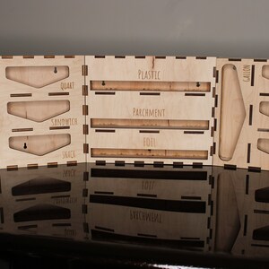 May include: Wooden organizer with slots for storing various sizes of plastic wrap, parchment paper, and aluminum foil. The organizer has labels for "Gallon", "Quart", "Sandwich", and "Snack".