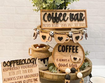 Peut inclure: Un plateau en bois à plusieurs niveaux avec des décorations sur le thème du café. Le niveau supérieur a une pancarte qui dit "Coffee Bar", le niveau du milieu a une pancarte qui dit "Coffee is always a good idea", et le niveau inférieur a une pancarte qui dit "Coffeeology Espresso Yourself Better Latte Than Never Always Stay Grounded So Many Blends, So Little Time Deja Brew".