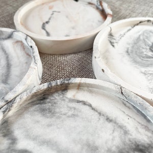 Pu&ograve; includere: Quattro sottobicchieri rotondi in marmo bianco con venature grigie e marroni. I sottobicchieri sono impilati uno sopra l'altro.