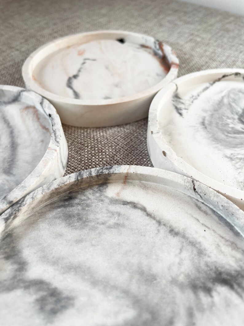 Pu&ograve; includere: Quattro sottobicchieri rotondi in marmo bianco con venature grigie e marroni. I sottobicchieri sono impilati uno sopra l'altro.