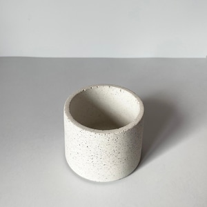 May include: A small, white, cylindrical concrete planter with a speckled texture.