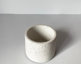 May include: A small, white, cylindrical concrete planter with a speckled texture.