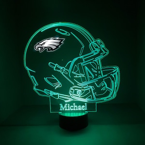 May include: A green illuminated 3D printed night light shaped like a football helmet with the Philadelphia Eagles logo on the side. The name "Michael" is printed on the base of the night light.