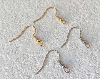 May include: Four earring hooks, two gold and two silver, on a white textured surface.